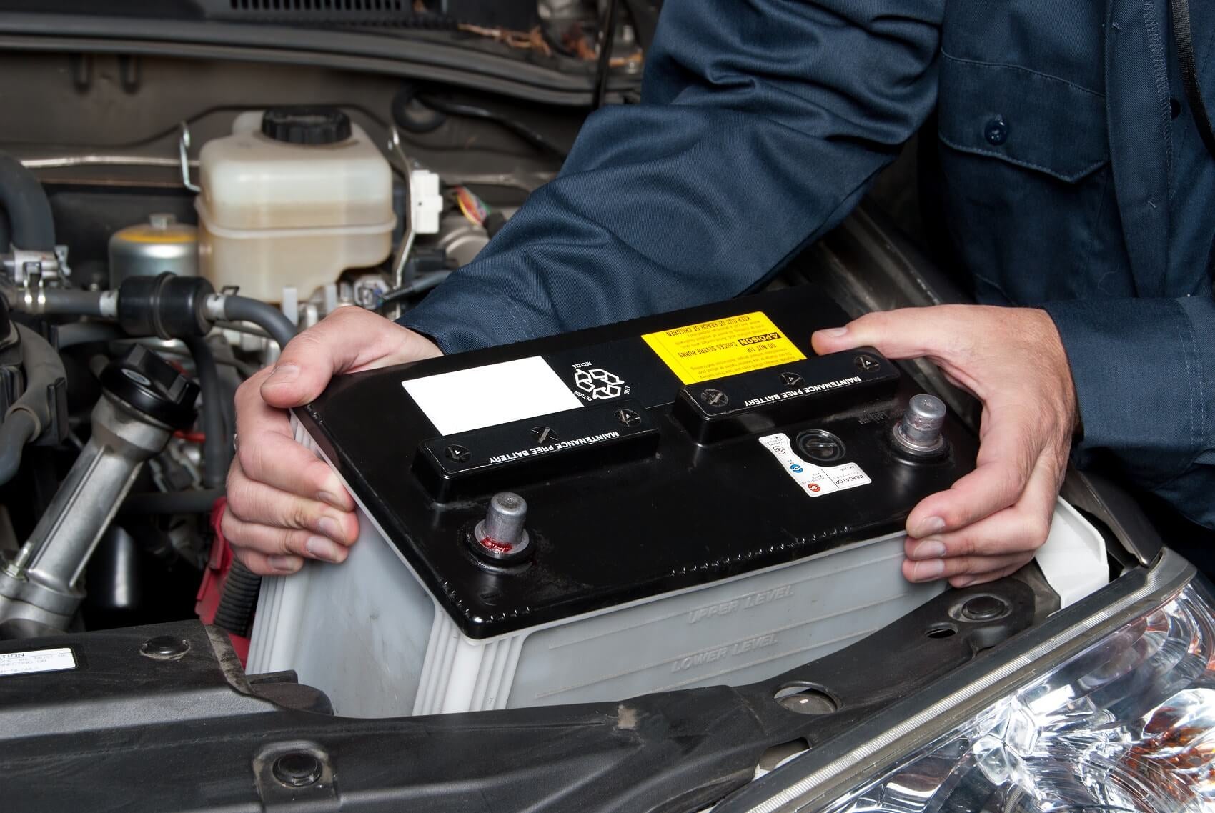 A technician holding a new battery that is about to be placed in a vehicle