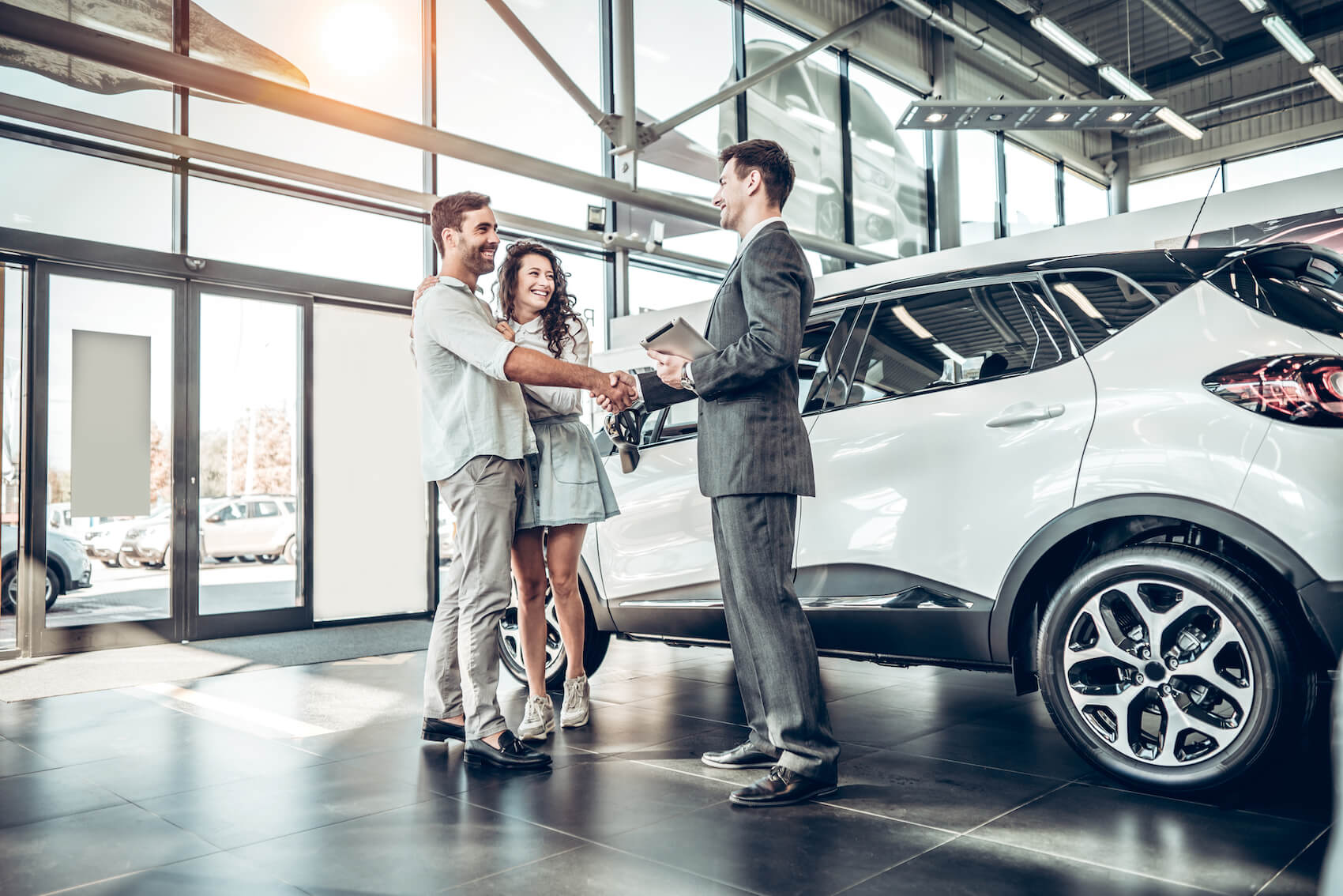 A car salesman shaking hands with a couple who just financed a white SUV at a car dealership